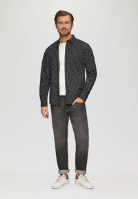 Zwarte shirt met witte stippen, gedragen over een wit t-shirt, gecombineerd met grijze jeans en witte sneakers. Glad stof en slim fit ontwerp.