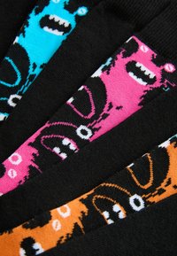 Chaussettes noires présentant des visages de monstres colorés en bleu, rose et orange avec des bouches ouvertes et de grands yeux disposés en diagonale.