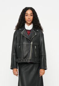 Μαύρη δερμάτινη μπουφάν μοτοσικλετιστή με ζώνη στη μέση, ασύμμετρο μπροστινό φερμουάρ, κουμπιά με κλιπ και φαρδιές πέτες. Υφή υλικού με μακριά μανίκια.