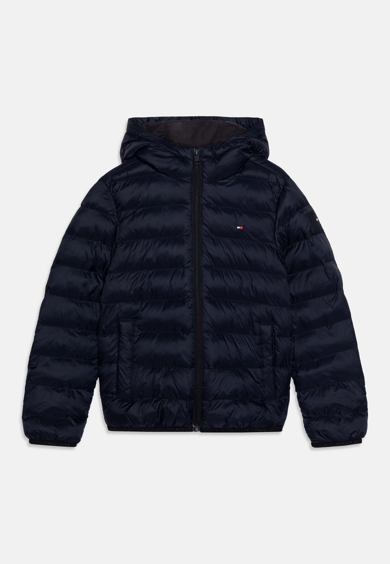 Ναυτική puffer ζακέτα με κουκούλα, φτιαγμένη από ένα λαμπερό, εσωτερικά γεμιστό ύφασμα. Διαθέτει φερμουάρ μπροστά, πλαϊνές τσέπες και ένα μικρό λογότυπο στο στήθος.