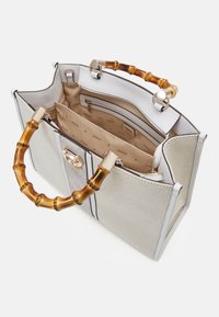 Large beige handbag with textured fabric, silver accents, and a bamboo handle. Interior features multiple pockets with a lined design.