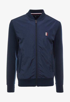 Marineblaue Bomberjacke mit Reißverschluss, gerippten Bündchen und Saum, ausgestattet mit einem kleinen Logo-Patch und Seitentaschen. Glatte Stoffqualität mit taillierter Passform.