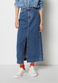 Jeansmaxkjol i medelblått, med en framknäppning och fållade kanter. Matchad med vita sneakers och orange strumpor.