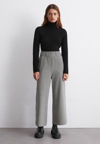 Schwarz gerippter Rollkragenpullover mit langen Ärmeln, kombiniert mit grauen karierte weiten Hosen mit elastischem Bund und schwarzen klobigen Stiefeln.