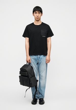 Μαύρο βαμβακερό μπλουζάκι με τσέπη με σχέδιο, ανοιχτό μπλε τζιν παντελόνι και μαύρο υφασμάτινο σακίδιο πλάτης με πολλαπλές θήκες.