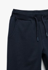 Mørkeblå sweatpants lavet af blødt stof, med ribbet talje, snøre og sidelommer til opbevaring.