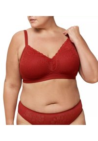Bralette en dentelle rouge avec motif floral, cups légèrement rembourrées, bretelles ajustables et bande inférieure lisse. Culottes assorties en dentelle rouge visibles en dessous.