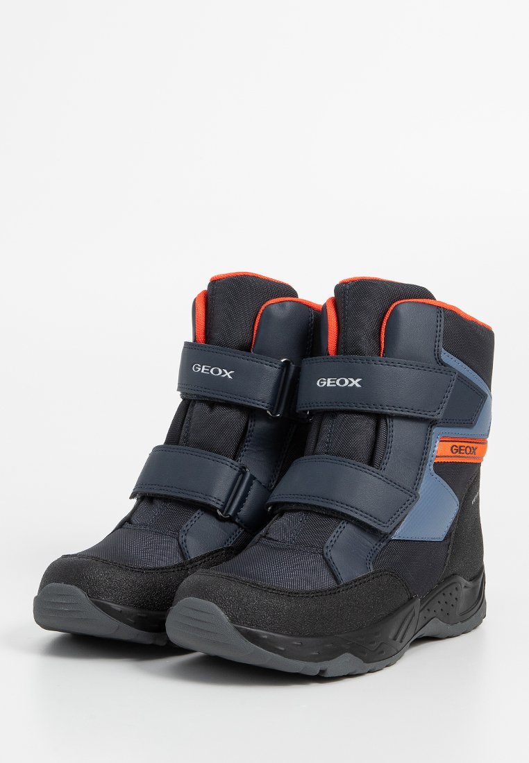 Dunkelblaue und schwarze Stiefel mit zwei Klettverschlüssen, aus Stoff und synthetischen Materialien, orangefarbigen Akzenten und einer strukturierten Sohle für besseren Halt.