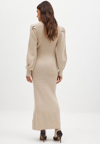 Stickad, beige midiklänning med ribbad textur, långa ballongärmar och slits på sidan, tillsammans med svarta högklackade skor.