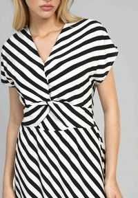 Robe rayée noir et blanc à manches courtes, avec un col en V et un détail torsadé à la taille. Tissu lisse, design jusqu'au genou.