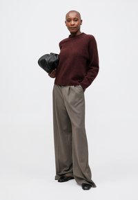 Tricou din lână bleumarin, pantaloni gri plisati lejeri și geantă neagră, completate de pantofi slip-on negri. Design simplu, modern.