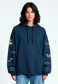 Marineblauwe hoodie met een front pocket, voorzien van kleurrijke borduursels: vlinders, harten en zinnen op de mouwen. Zachte, casual pasvorm.