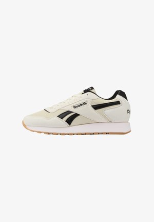 Zapatilla Reebok blanca y negra con suela de goma, logo lateral, diseño con cordones y collar acolchado sobre fondo blanco.