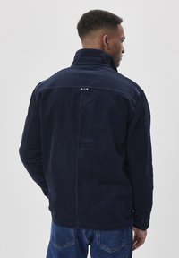Jachetă din catifea navy cu guler înalt, textură ribbed și detalii cu nasturi prin presiune. Partea din spate are o cusătură orizontală și două embellishments subtile.