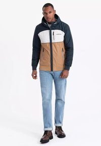 Farbblockierte Jacke mit navy, weißen und braunen Einsätzen. Inklusive Kapuze, vorderem Reißverschluss und zwei Reißverschlusstaschen. Glatte Stoffoberfläche.