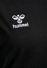White hummel logo with stylized bee and text embroidered on black fabric background.