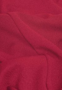 Tessuto rosso, texture liscia, con sottili variazioni di tonalità. Il materiale appare morbido e flessibile, drappeggiandosi leggermente.