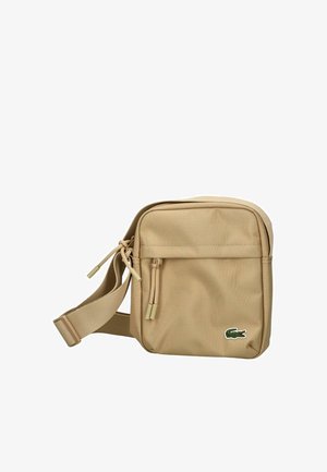 Bolso cruzado beige con correa ajustable, bolsillo frontal con cremallera y pequeño logo de cocodrilo verde en la esquina inferior derecha.