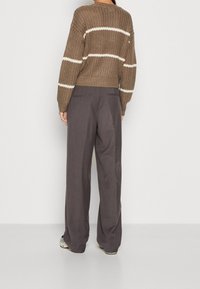 Sweter dzianinowy w brązowym kolorze z białymi paskami oraz luźne szare spodnie. Sweter ma ściągacz na dole i opadające ramiona.