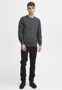 Suéter de punto gris carbón con cuello redondo, hecho de material suave, con mangas y cintura ajustadas. Combinado con jeans skinny negros y zapatos casuales.