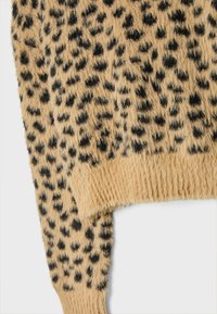 Flauschiger beiger Stoff mit schwarzen Punkten, mit einem gerippten Saum. Die Textur wirkt weich und plüschig, geeignet für ein gemütliches Kleidungsstück.