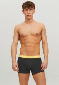 Schwarze Boxershorts mit einem gelben elastischen Bund, auf dem der Markenname "JACK & JONES" in Weiß gedruckt ist. Weicher, dehnbarer Stoff.