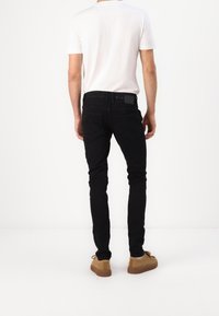 Jeans negros ajustados con una textura suave, cuatro bolsillos y un lazo para el cinturón. Combinados con una camiseta blanca sencilla y zapatos de ante marrón.