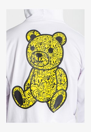 Sweatshirt à capuche blanche avec un grand motif de ours en peluche jaune au dos, rehaussé de contours noirs et de motifs abstraits.
