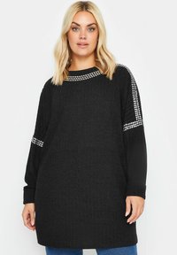 Svart ribbad tröja med långärmar, med rund halsringning och silverfärgade nitar på axlarna. Texturerad tyg, avslappnad passform.