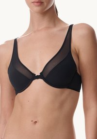 Svart bh med genomskinliga meshpaneler, underwire-stöd och justerbara axelband. Har en framknäppning och slät textur.