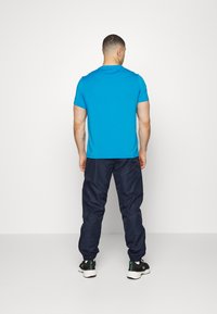 Turkise t-skjorte med korte ermer, marineblå joggebukser med elastiske mansjetter, og svarte joggesko med hvite såler, sett fra baksiden.