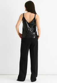Black sequined top with a V-back design, thin straps, and a flowy silhouette, paired with loose black pants. Smooth, shiny texture.