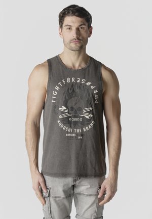 Hombre con camiseta sin mangas gris oscuro con gráfico de calavera y llamas, pantalones cortos cargo gris claro, de pie contra un fondo liso.