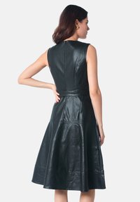 Robe en cuir noir avec un corsage ajusté, une jupe évasée et une fermeture éclair au dos. Elle présente une texture lisse et des coutures verticales subtiles.