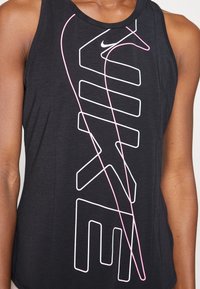 Camiseta atlética negra sin mangas con un destacado logotipo blanco de "NIKE" con un contorno rosa. Fabricada con un material suave y ligero.