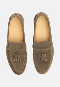 Braune Wildleder Slipper mit Quastenakzent, runder Zehenform und kontrastierenden Nähten. Glatte Innenauskleidung.