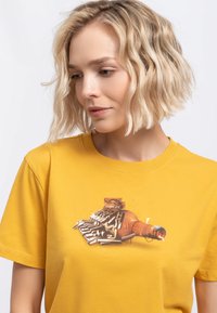 T-shirt en coton jaune avec un imprimé graphique représentant une bouteille et un design de clavier, avec des couleurs vives et des textures détaillées.