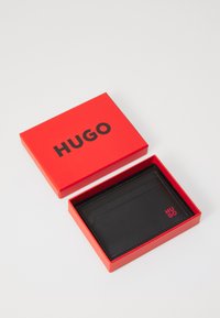 Portofel din piele neagră într-o cutie roșie cu logo-ul "HUGO". Portofelul dispune de mai multe sloturi pentru carduri și un design elegant, minimalist.