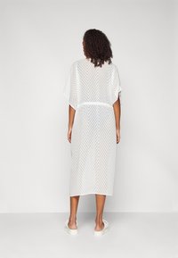 Kimono bianco trasparente con motivo a zigzag, taglio morbido, vita dotata di cintura, lunghezza a metà polpaccio, maniche corte e texture liscia.