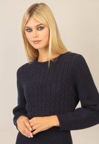 Granatowy sweter w splot kablowy z okrągłym dekoltem, teksturowanym wzorem na korpusie i ściągaczami przy rękawach. Miękka tkanina o dopasowanym kroju.
