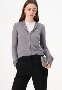 Grå ull cardigan med V-hals, frontknapper og ribbede mansjetter. Har liten "2NDDAY" brodering på venstre bryst. Svart skreddersydde bukser.