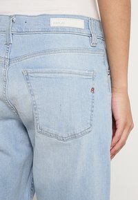 Hellblaues Denim-Jeans, ausgestattet mit einer Gesäßtasche mit rotem "R"-Stickerei, klassischem Fünf-Taschen-Design und einem Markenlabel am Bund.