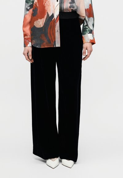 Pantalon à jambes larges en velours noir à texture lisse, assorti à un chemisier floral coloré aux nuances de rouge, vert et gris.