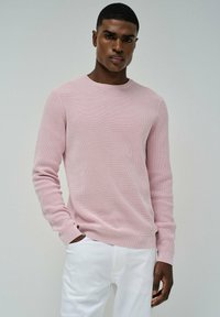 Maglione a coste rosa chiaro con scollatura rotonda e maniche lunghe, abbinato a pantaloni bianchi. Texture morbida, design minimale e forma aderente.