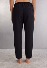 Pantaloni neri a vestibilità comoda con vita elasticizzata e una tasca posteriore. Tessuto liscio, lunghezza alla caviglia.