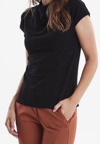 Černý krátký rukáv top s kulatým výstřihem, vyrobený z hladkého materiálu. V kombinaci s hnědými kalhotami se bočními kapsami a slim fit střih.