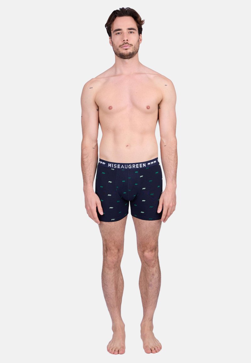 Boxer-culottes bleu marine avec une texture douce, présentant un motif répété de petits ours verts et blancs. La ceinture est marquée "Miseaugreen."