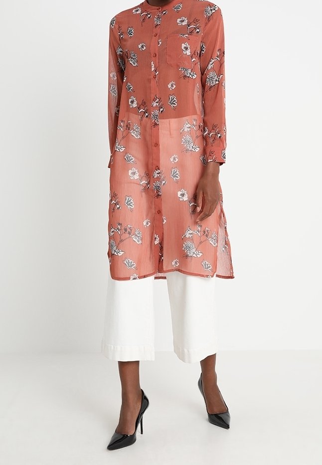 Rose-colored sheer blouse with floral pattern, button-down front, long sleeves, and single chest pocket. Paired with wide white trousers.