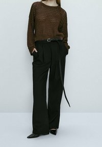 Pull en tricot marron à coupe décontractée, assorti à un pantalon noir taille haute et une ceinture tressée noire, le tout complété par des chaussures noires à bout pointu.