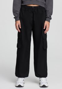 Pantaloni cargo neri con un elastico in vita, dotati di due ampie tasche laterali. Mostrati con una felpa grigia corta e sneakers bianche.